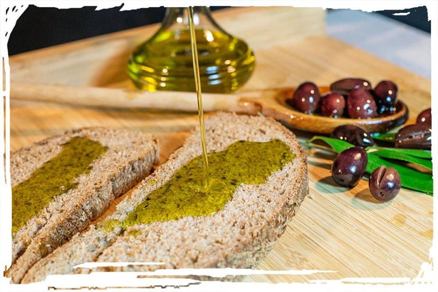 olive oil flowed on slices of bread at Elladiko with bowl with black olives in the background